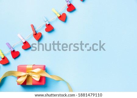 Happy Valentine's day concept. red heart-shaped valentines decoration hanging with clips for love and red gift box with golden ribbon on the rope greeting card on blue background with copy space