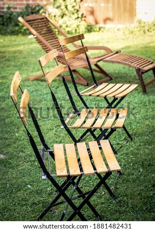 A vertical image of three wooden chairs and lounge chair on a lawn