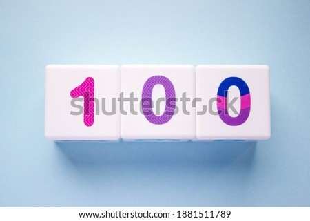 Close-up photo of a white plastic cubes with a colorful number 100 on a blue background. Object in the center of the photo