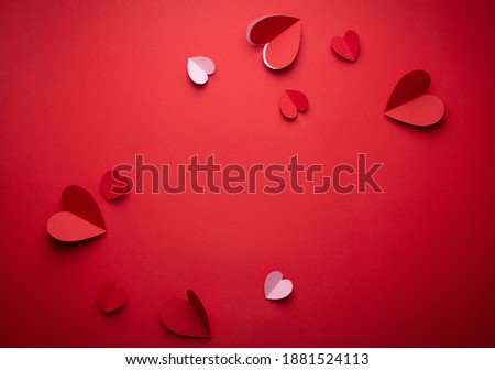 Red and pink hearts cut from paper on red monochrome background, paper craft origami style, from above. Romantic Valentine's day backdrop, love concept. Paper trendy art design, space for text

