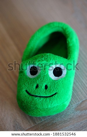 A vertical shot of a soft green slipper with a face on it for kids