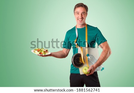 Man dressed in sportswear with meter scale and water and salad plate on green isolated gradient background Royalty-Free Stock Photo #1881562741