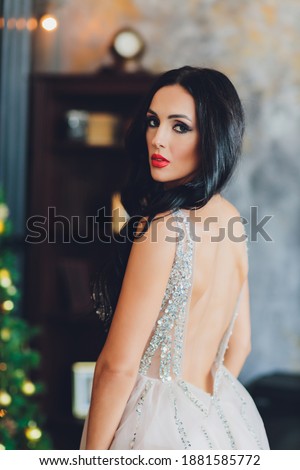 Beautiful woman girl in new year's studio posing, photo new year photo session. Beautiful girl in a luxurious dress with slender legs. Christmas, winter, happiness concept.