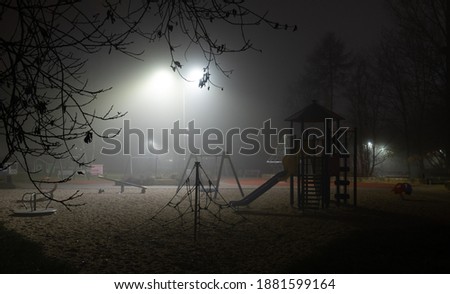 Abandoned playground by night. Illuminated by street lamp from background.