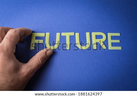 Human fingers holding the word Future written with plastic letters on blue paper background, concept