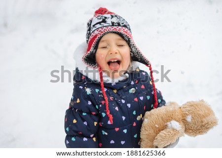 Cute little girl in winter clothes catching snowflakes with her tongue during a snowfall.