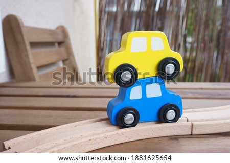 A blue and a yellow wooden car toys on tracks with a blurred background