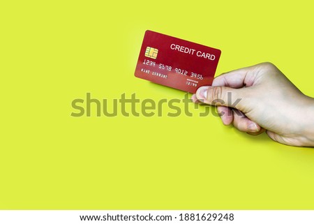 Hand holding a red credit card on a yellow background, credit card can be used to pay for goods or services, credit card concept. Credit card clipping path.