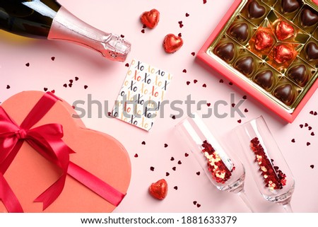 Valentines Day flat lay composition. Top view box of chocolates, heart shaped gift box, champagne bottle and glasses, greeting card and confetti on pink table.