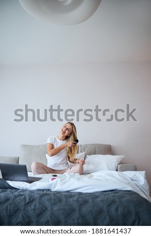 Full length portrait of happy smiling blonde Caucasian woman in sleepwear enjoying weekend in bedroom at home