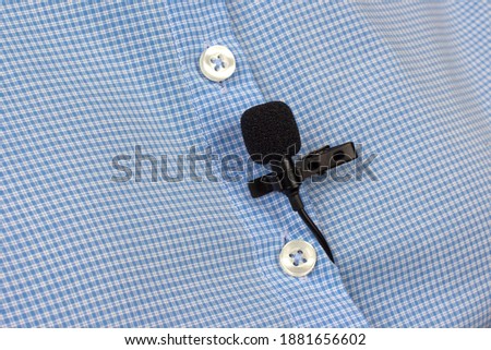 The lavalier microphone is secured with a clip on a women's shirt close-up. Audio recording of the sound of the voice on a condenser microphone
