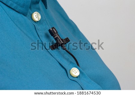 The lavalier microphone is secured with a clip on a women's shirt close-up. Audio recording of the sound of the voice on a condenser microphone