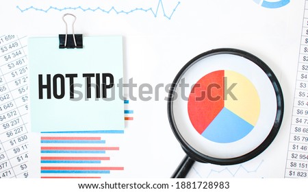 Green card on the white notepad and magnifier on the financial documentation. Text Hot tip. Business concept
