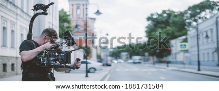 Director of photography with a camera in his hands on the set. Professional videographer at work on filming a movie, commercial or TV series. The filming process on the street, on location Royalty-Free Stock Photo #1881731584