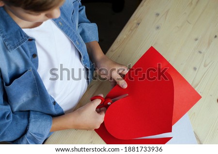 Teen boy making of handmade  greeting card with scissors and red paper,Valentine's Day, Mother's Day DIY Ideas for children. Love and child art hobby concept. Gift with your own hands, red paper heart