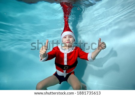 A picture of a boy smiling underwater in a Santa Claus costume in the pool. Active happy child. Healthy lifestyle. A swimming school. Athletics. The concept of the celebration
