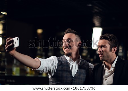 two friends meet in a bar and take a selfie on their smartphone.