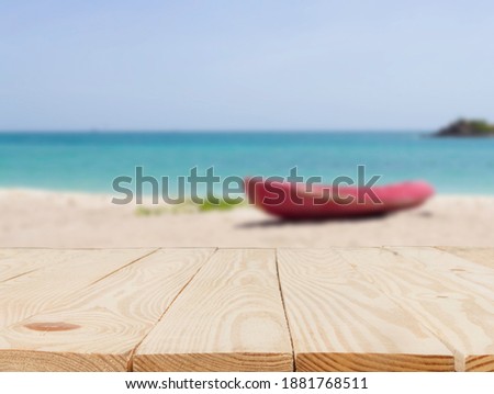 wooden table in front of abstract blurred in view of the red boat on the beach and sky background