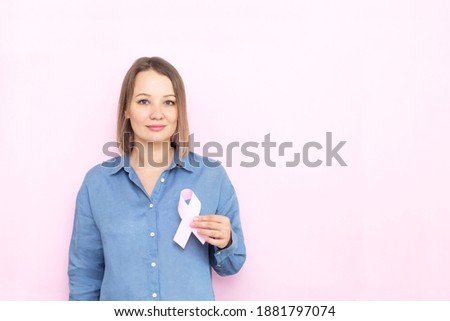 Young woman holding brest cancer ribbon over pink background.