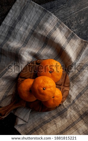 group of orange tangerines on a wooden old table lie on a striped napkin, dark photo