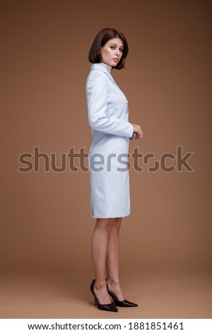 Fashion photo of a beautiful elegant young woman in a pretty blue suit in the style of a flight attendant stewardess, pearl necklace posing over brown background. Bob haircut. Studio Shot. 
