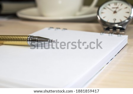 The yellow pen lies on a white notebook that is on a blurry background of a wristwatch and a white Cup. Concept photo