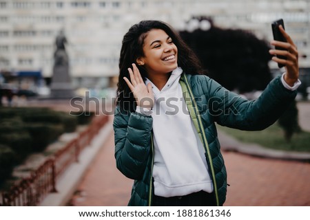 Young african woman student taking selfie on her smartphone outdoors on autumn street