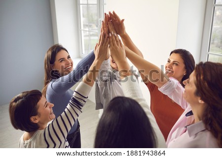 Team of happy confident smiling young women standing in circle and putting hands together, feeling united and empowered. Concept of unity, support, success and reaching common business goal together Royalty-Free Stock Photo #1881943864