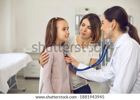 Mother and child at medical checkup at hospital or clinic. Friendly female doctor listening to young patient's breath or heartbeat. Smiling pediatrician with stethoscope checking little girl's lungs Royalty-Free Stock Photo #1881943945