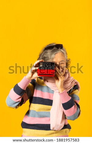 Senior woman in casual clothes taking a picture with an instant camera against a yellow background