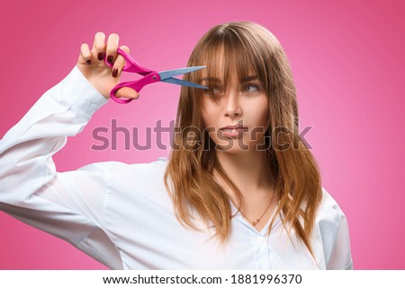 Young beautiful girl stylist makes her hair with scissors. Fashionable bangs in 2021. Stylish hairstyle with your own hands. Woman hairdresser at work Royalty-Free Stock Photo #1881996370