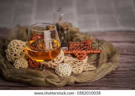 Warm and cozy still-life picture with soft fabric, cognac\brandy glass, some new year\christmas decoration and "Welcome" title made of wooden letters. Vintage newspaper and plank table in background.
