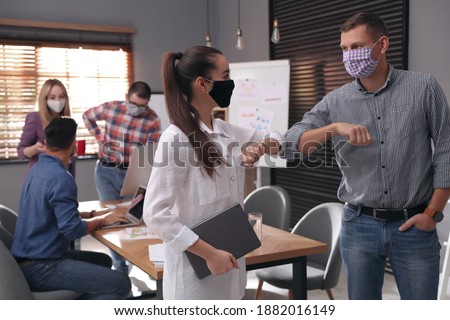 Coworkers with protective masks making elbow bump in office. Informal greeting during COVID-19 pandemic Royalty-Free Stock Photo #1882016149