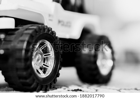 A greyscale closeup shot of the wheels of a toy car on the carpet