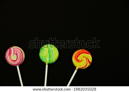 Round multicolored lollipops on a black isolated background, minimalistic photo, flat design, copy space