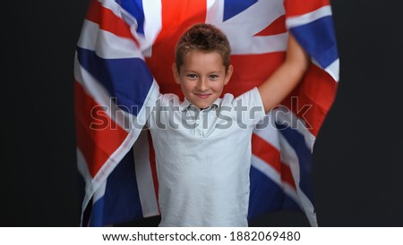 Happy little boy holding the flag of England or Great Britain, celebrating independence day expresses patriotism isolated on black background.  Royalty-Free Stock Photo #1882069480