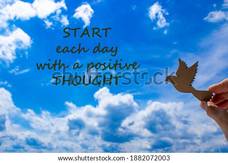 Man hand holding wooden bird on cloud sky background. Words 'start each day with a positive thought'. The development of the imagination, copy space. Motivational and business concept.
