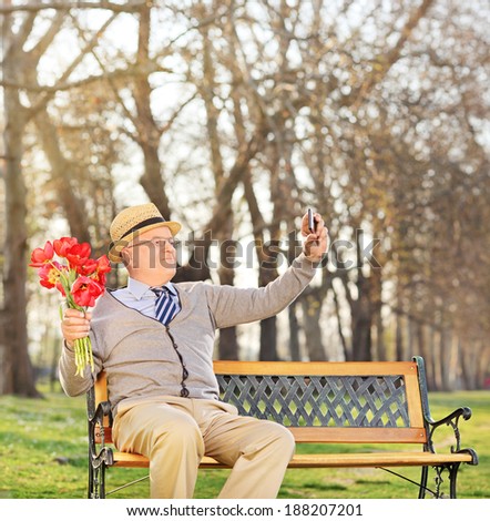 Senior holding flowers and taking selfie in park shot with tilt and shift lens