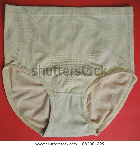 close beige seamless high-waisted women's underpants lie on a red background top view . women's panties with microfiber