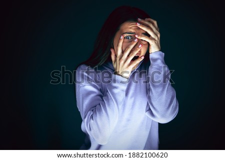 Hiding. Portrait of young crazy scared and shocked caucasian woman isolated on dark background. Copyspace for ad. Bright facial expression, human emotions concept. Looking horror on TV, cinema. Royalty-Free Stock Photo #1882100620