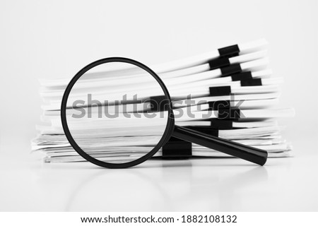 Stack of report paper documents with magnifying glass. Concept of business and search.