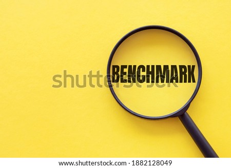 The word BENCHMARK is written on a magnifying glass on a yellow background. Royalty-Free Stock Photo #1882128049