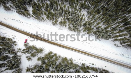 Winter road and red car in pine forest next to Hautes Gorges de la Riviere Malbaie National park, Quebec, Charlevoix, Canada, picture taken from drone