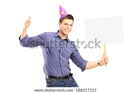 Handsome guy with party hat holding a blank panel and giving thumb up isolated on white background