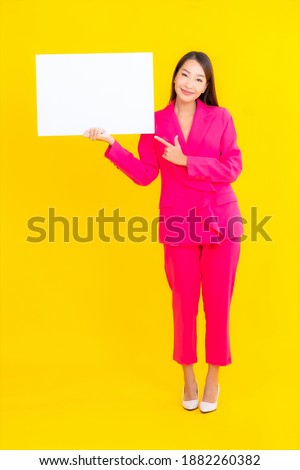 Portrait beautiful young asian woman with empty white billboard on yellow isolated background