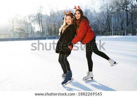 Two pretty girls one of whom is holding the other have fun ice skating in the park.