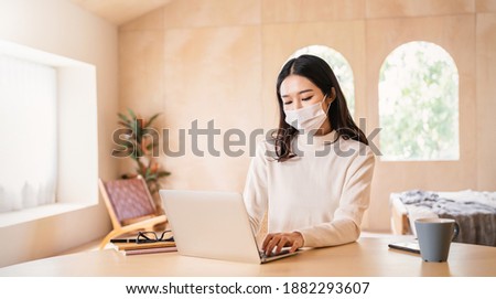 Portrait of sme business asian woman wears medical protective mask working from home at the computer desktop. Self isolation quarantine in winter. Coronavirus lockdown and flu covid epidemic. Royalty-Free Stock Photo #1882293607
