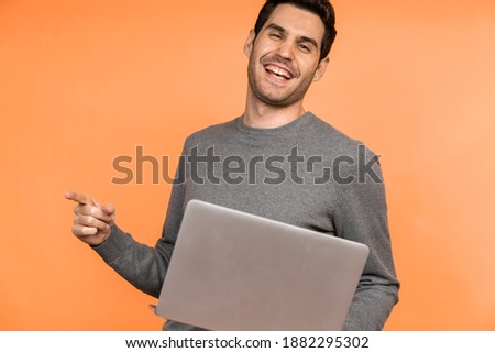 A young Caucasian male smiling and holding a laptop against an orange background