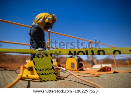 Safety workplace yellow striped caution tape warning sign barricade exclusion zone preventing from public access while defocused construction worker welder welding repairing fence      Royalty-Free Stock Photo #1882299523