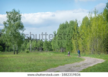 In summer, on a bright sunny day, brother and sister ride bicycles in the meadow along the road.